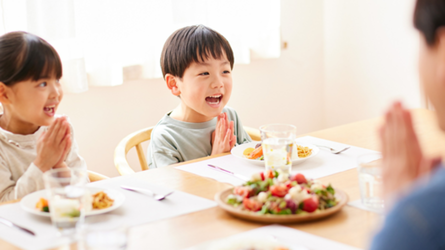 食卓に座った幼い男の子と女の子が、手を合わせて『いただきます』をしている様子
