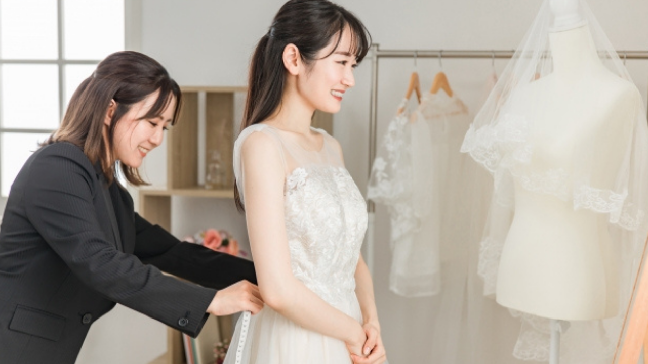 ウェディングドレスを試着する女性と、ドレスコーディネーターの姿。