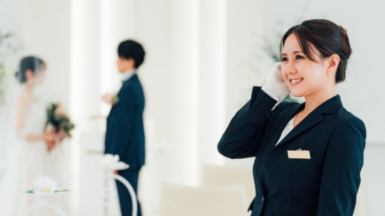 添付ファイルの詳細
ウェディングプランナーの姿。背景には向かい合って立つ新郎新婦の姿。