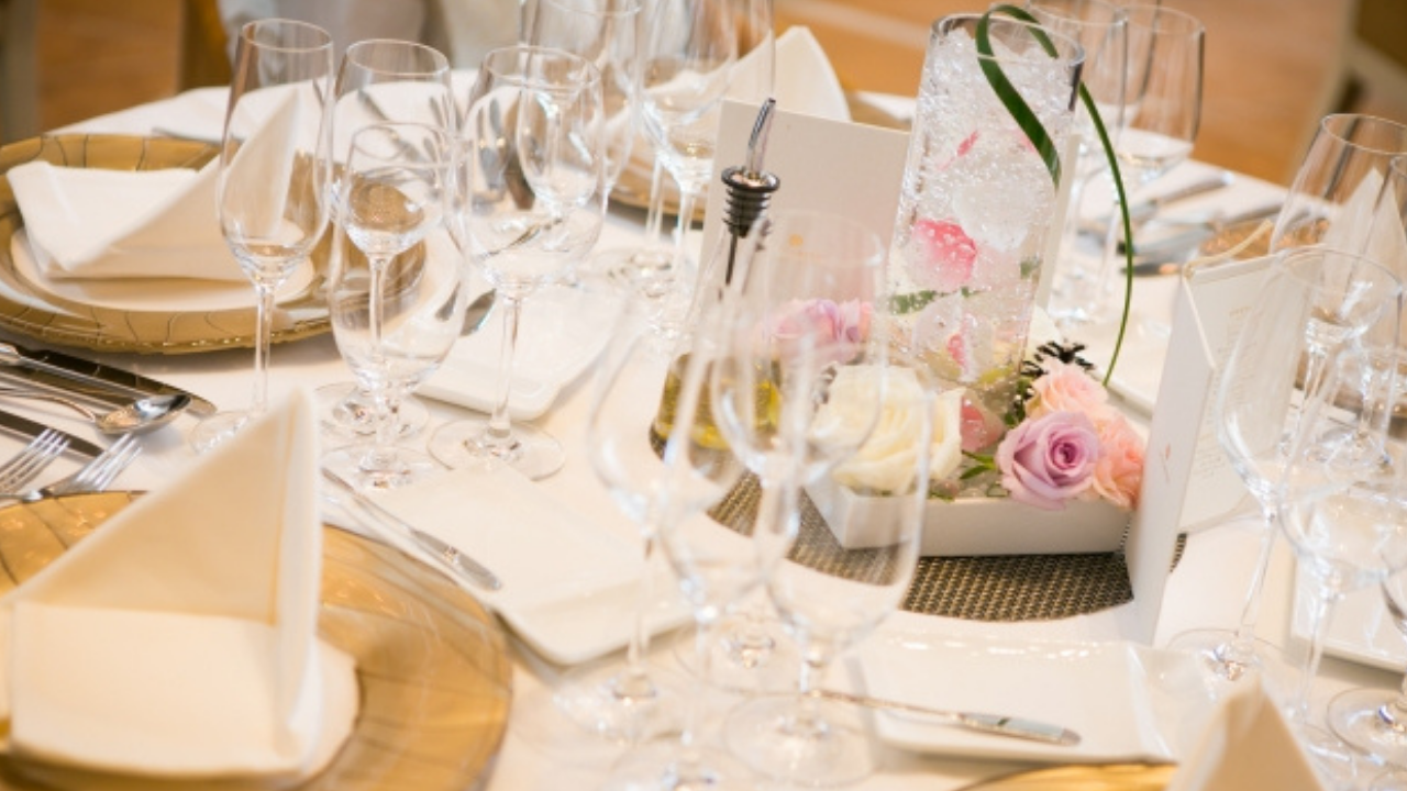披露宴会場の華やかにセッティングされたテーブルと装花、並べられたグラスやナイフフォーク。